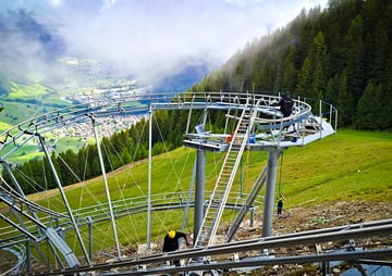 Achterbahn auf einer grünen Bergwiese mit Blick auf ein Tal