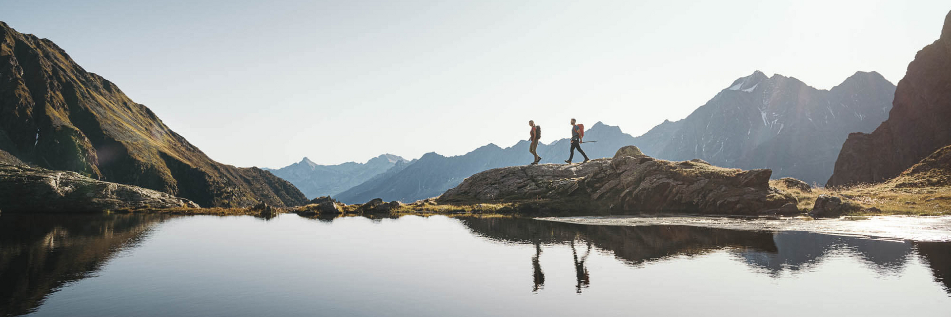 Zwei Personen wandern entlang eines Bergsees im Stubaital