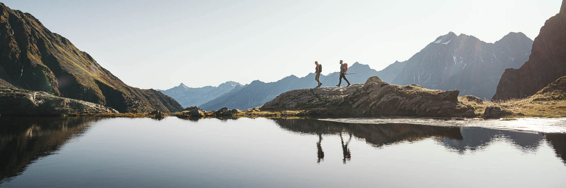 Zwei Personen wandern entlang eines Bergsees im Stubaital