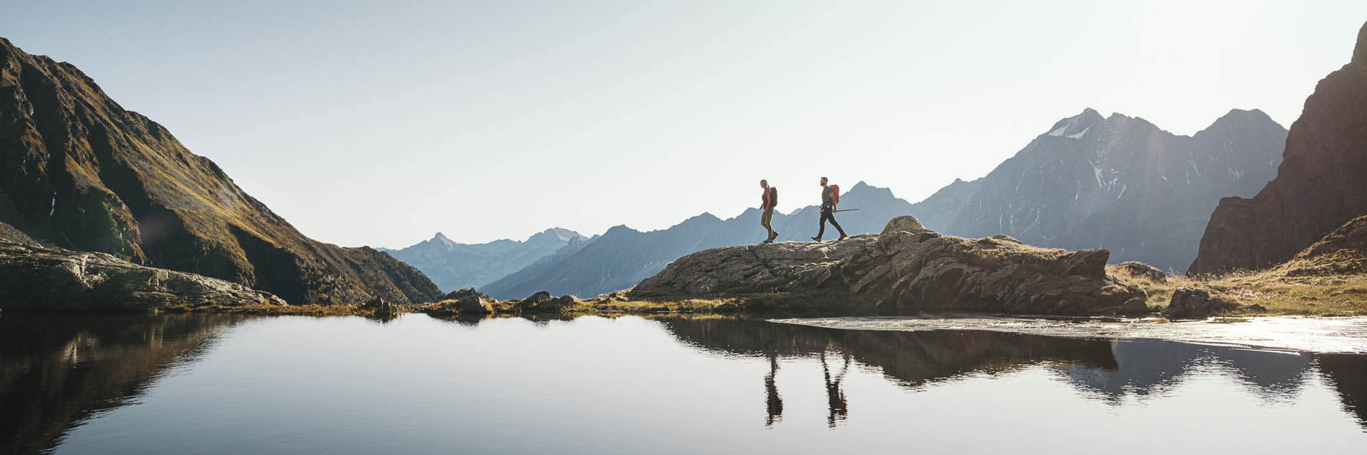 Zwei Personen wandern entlang eines Bergsees im Stubaital