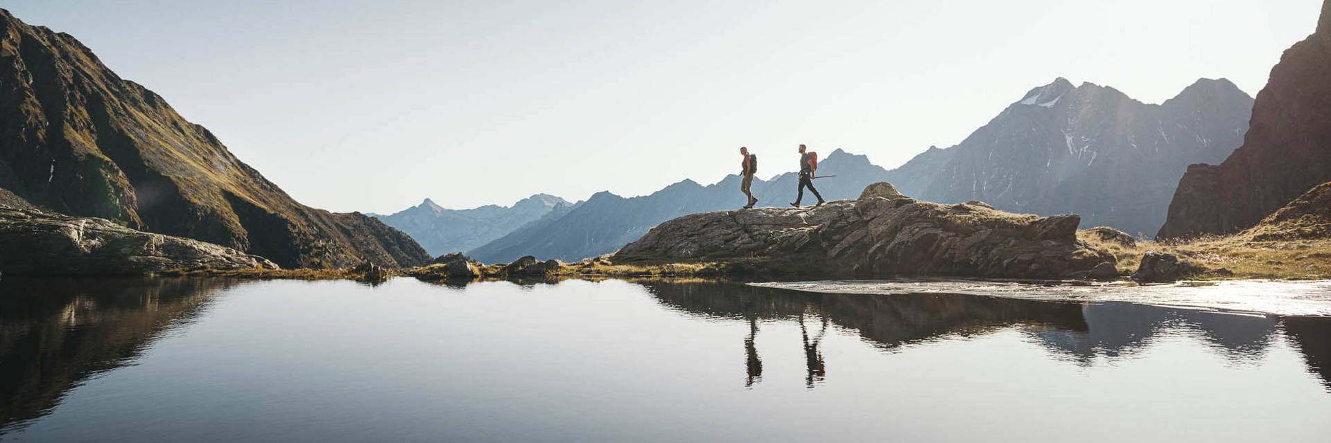 Zwei Personen wandern entlang eines Bergsees im Stubaital