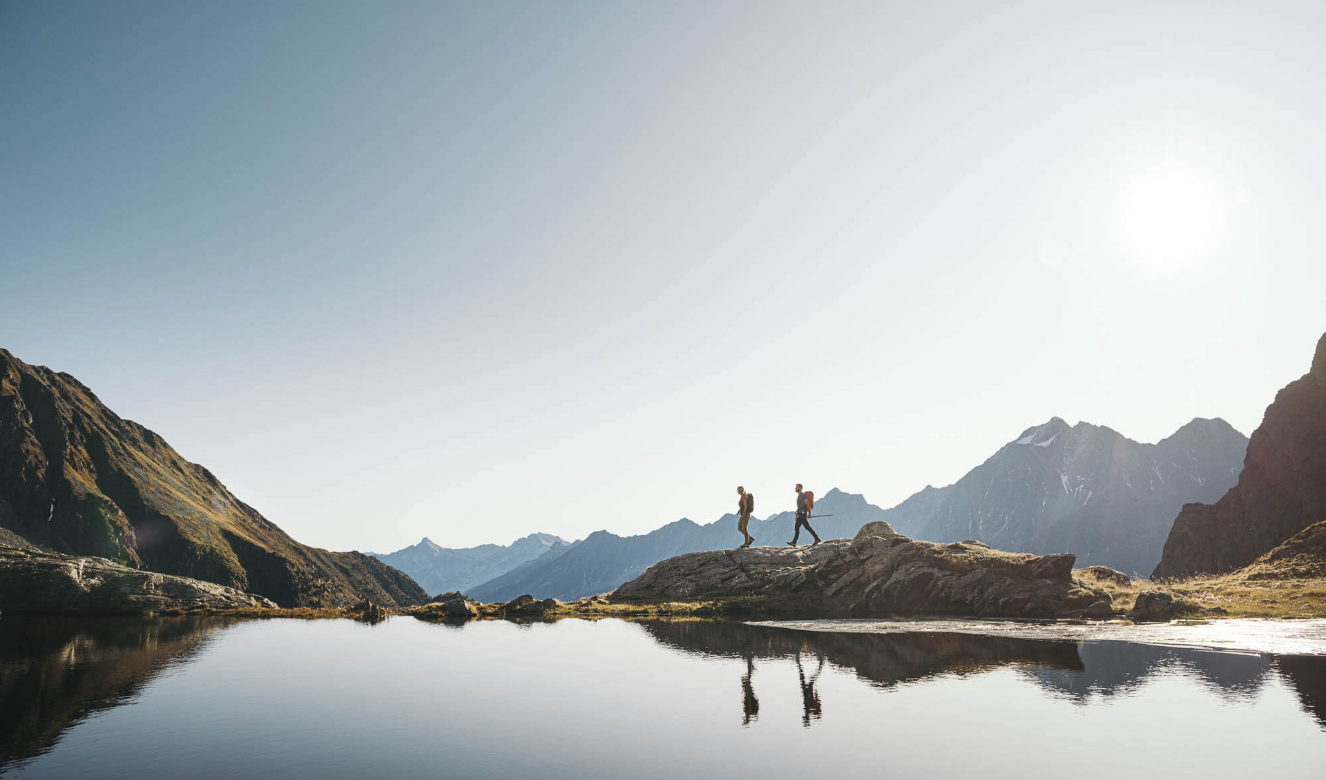 Zwei Personen wandern entlang eines Bergsees im Stubaital