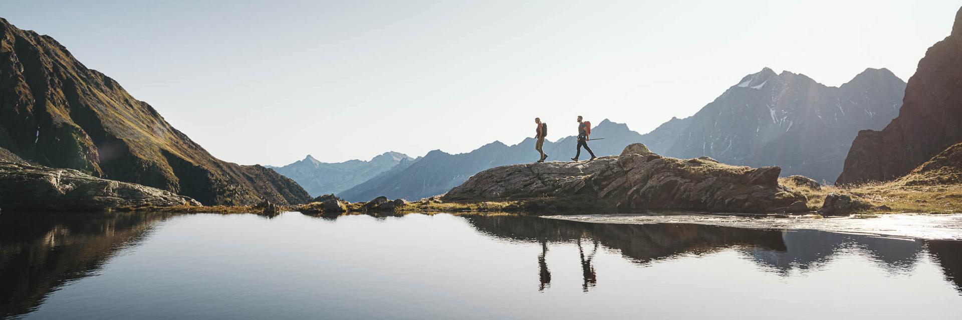 Zwei Personen wandern entlang eines Bergsees im Stubaital