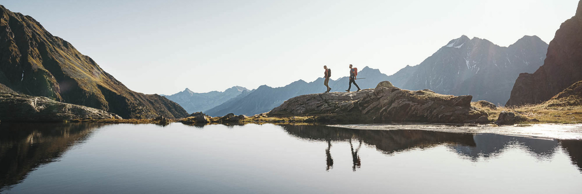 Zwei Personen wandern entlang eines Bergsees im Stubaital