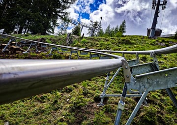 Blick entlang einer Schiene einer Sommerrodelbahn auf einer grasbewachsenen Anhöhe